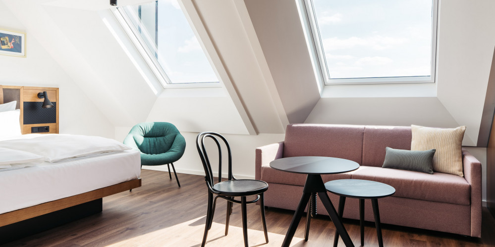 Eine Sitzecke mit Sofa, Tisch und Stuhl unter einem Fenster der Dachschräge im Hotel Schani