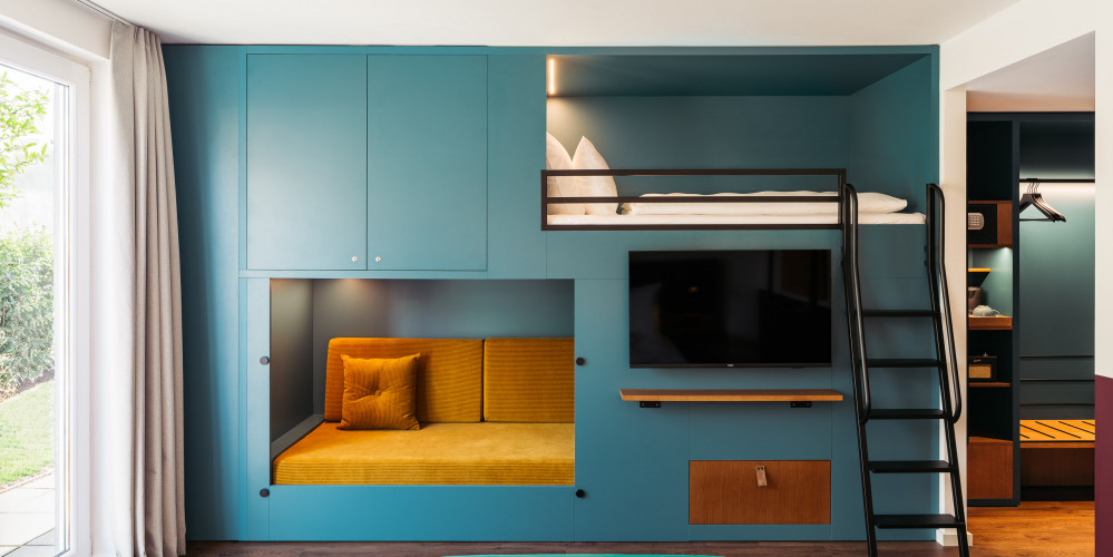 Ein Einbauschrank mit integriertem Hochbett, Sofa und Fernseher in Petrol im Familienzimmer in Wien