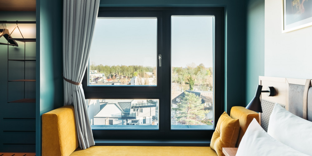 Eine Fensterbank zum Sitzen mit Senfgelben Polster an einem Fenster mit Blick auf eine Stadt